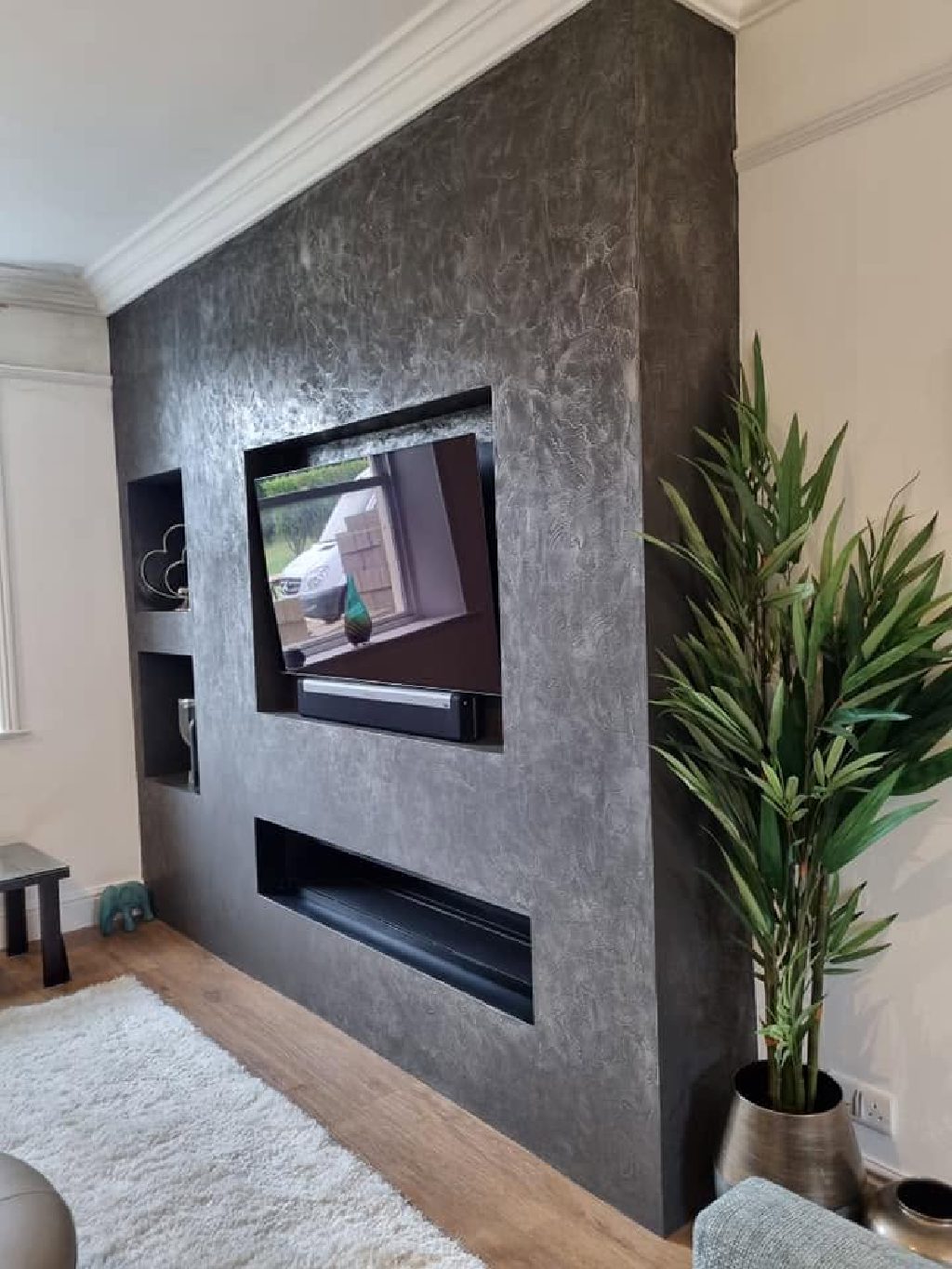 The pure nickel feature wall with the recessed television and the fire below