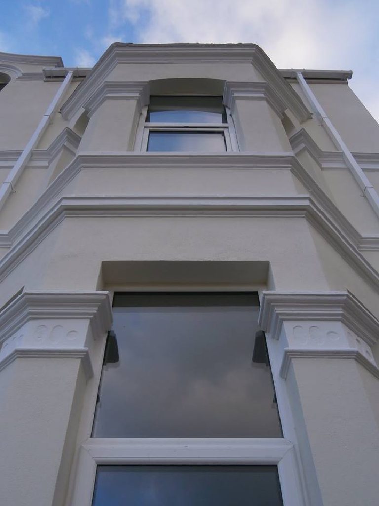 The front bay from below, corbels and moulded heads crisp against a blue sky