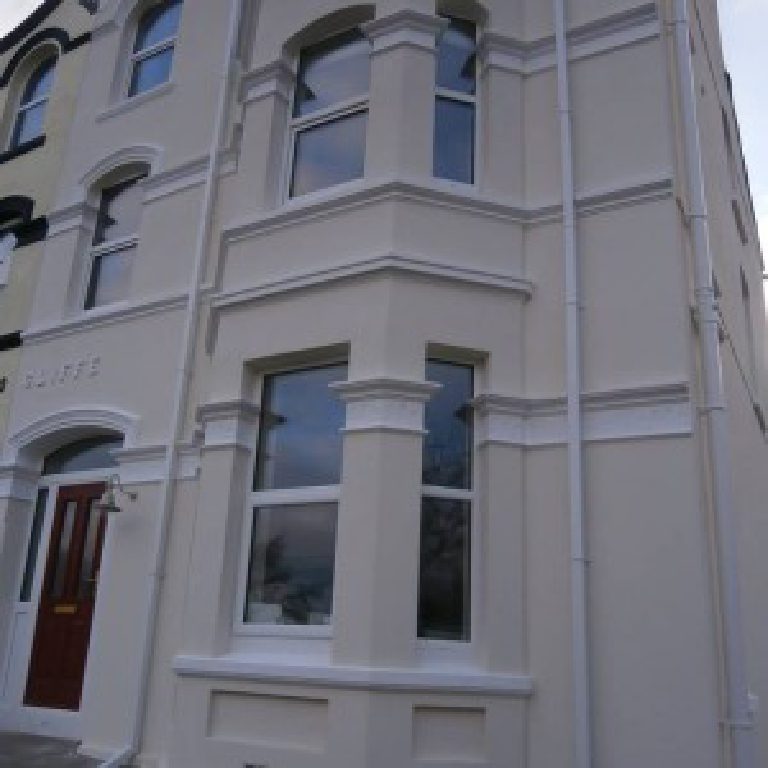 The front elevation from the pavement, red front door alongside the bay