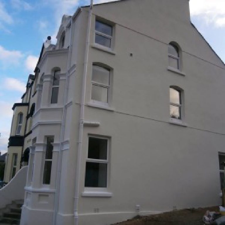 The gable end of the house, arched windows and smooth render down to bare ground