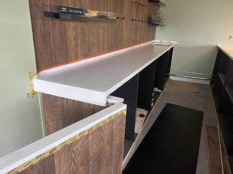 The bar top at base coat stage, plain and pale, with orange tape masking the timber wall behind