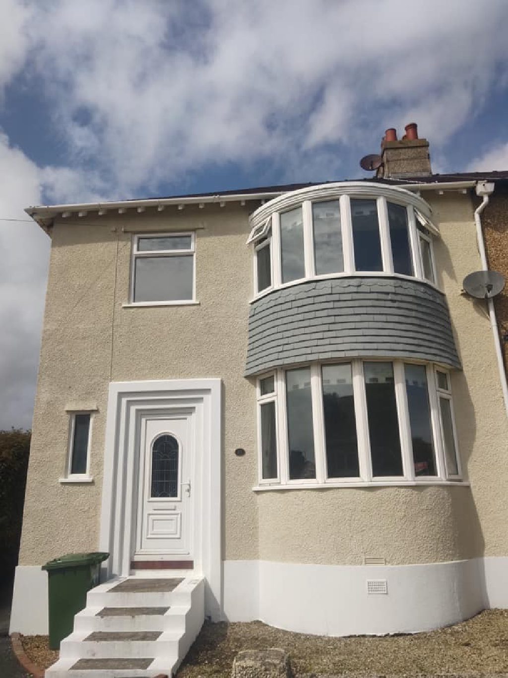The finished front elevation in cork render, taken in the sun, with the bay window and white plinth