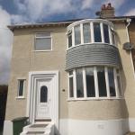 The finished front elevation in cork render, taken in the sun, with the bay window and white plinth