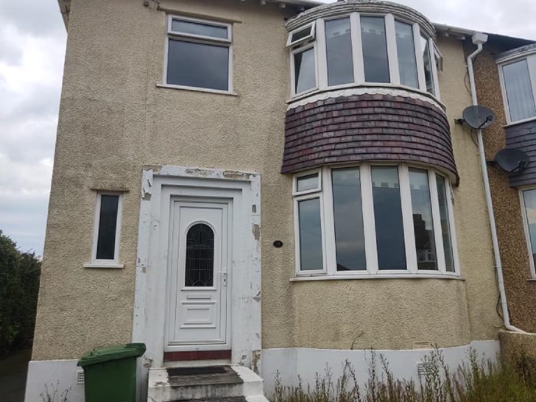 The front of the property before, seen at an angle, paint flaking from the door surround and weeds along the base