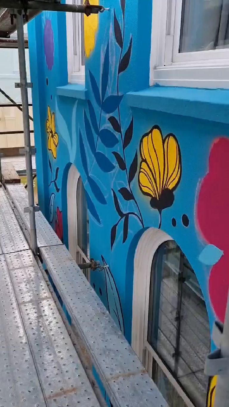 The mural part painted on the turquoise base, scaffold boards running along the elevation
