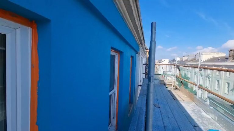 The turquoise rendered elevation running away along the scaffold lift, rooftops beyond
