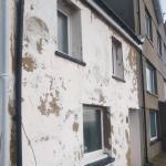 The same wall before the work — render blown off in patches down to the brown coat beneath