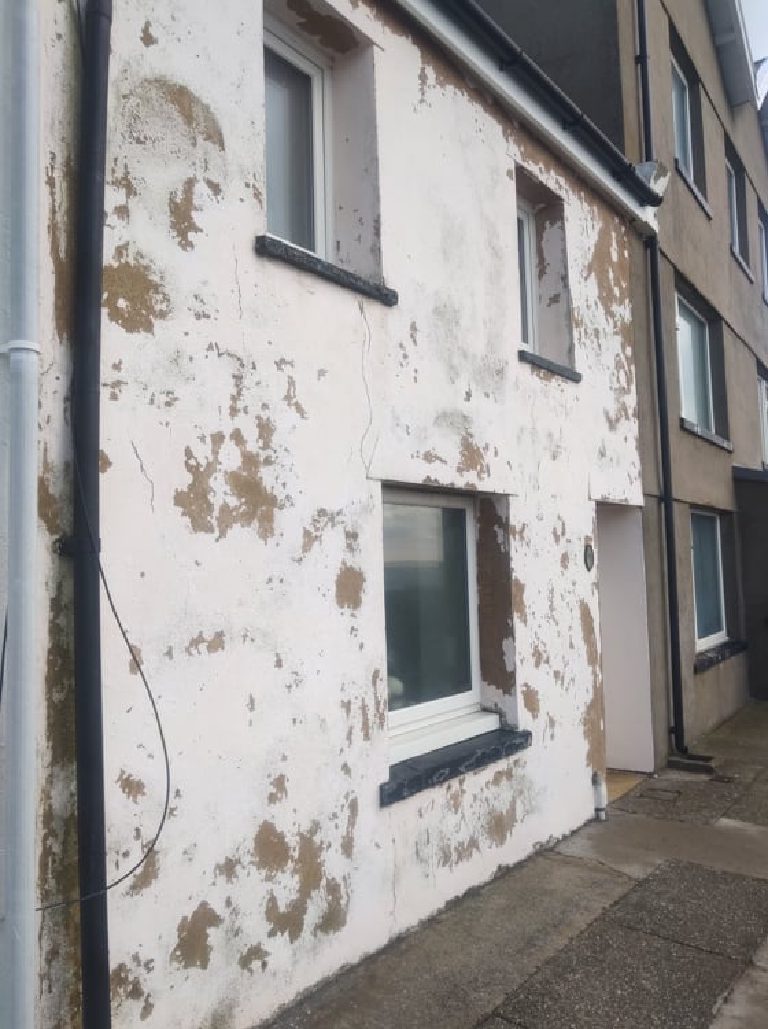 The wall before the work, the white coat blown off in patches with a crack running down beside the window