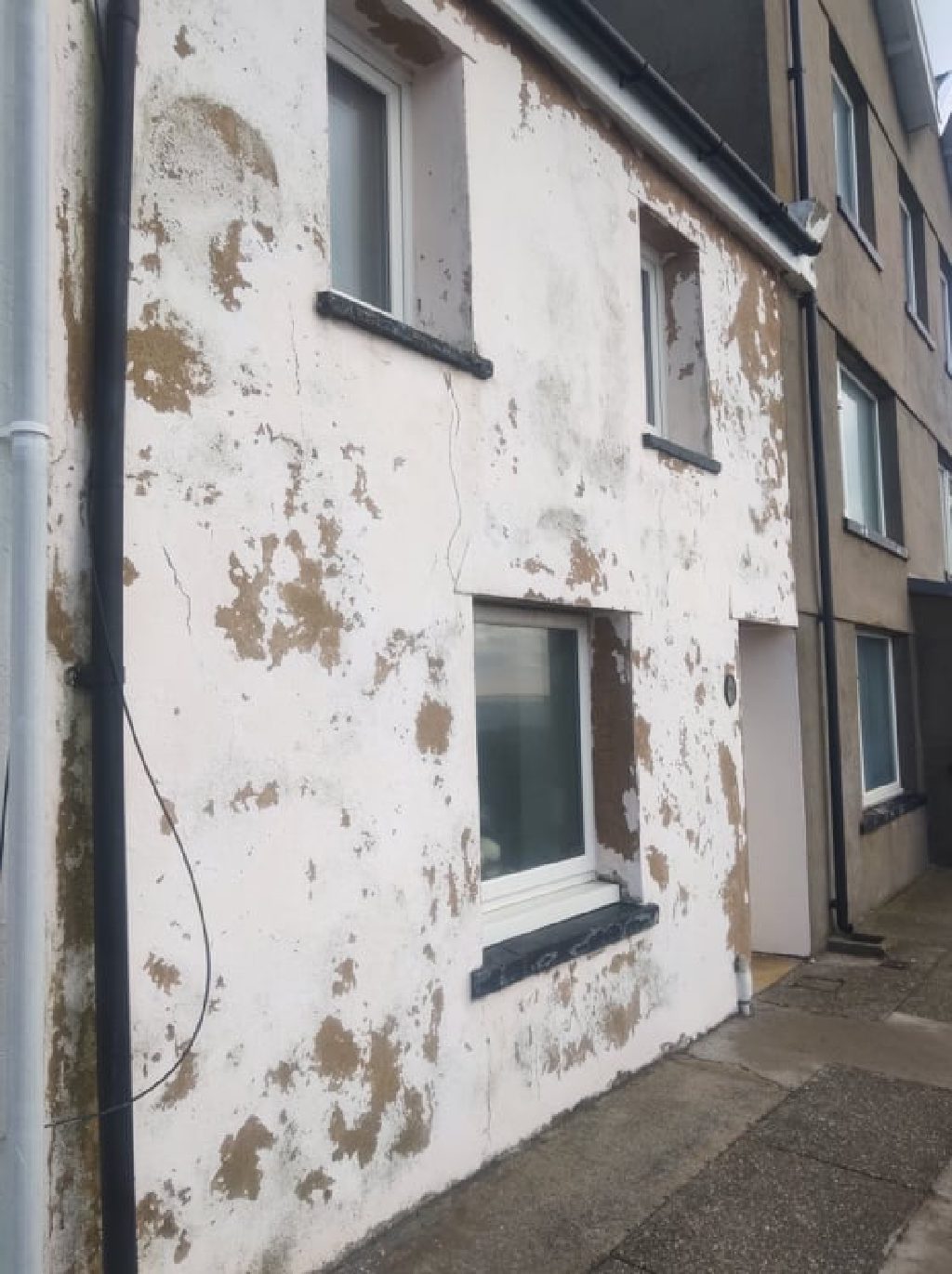 The same wall before the work — render blown off in patches down to the brown coat beneath