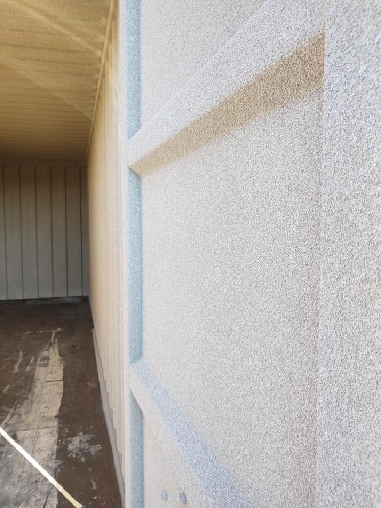The sprayed door leaf seen edge-on, with the container interior and its plywood floor beyond
