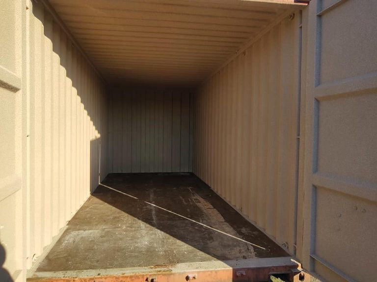 The inside of an untreated container — plain steel walls and ceiling, bare timber floor, rust on the door sill
