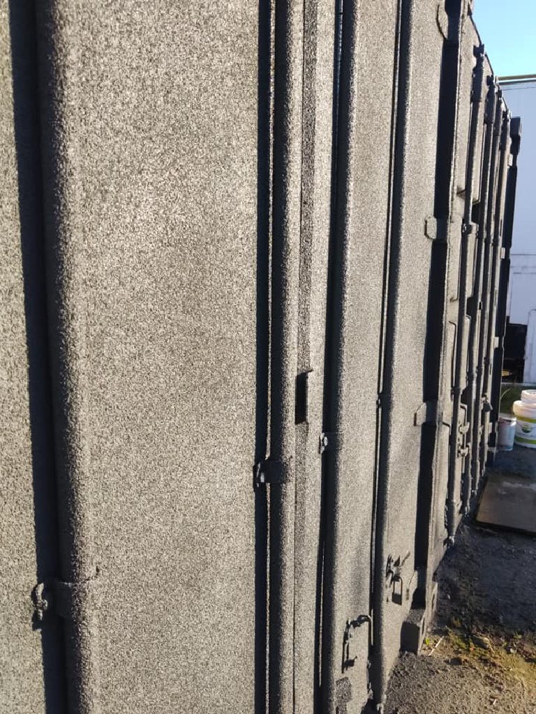 The doors end of a container sprayed grey, with the hinges, locking bars and cam handles all coated