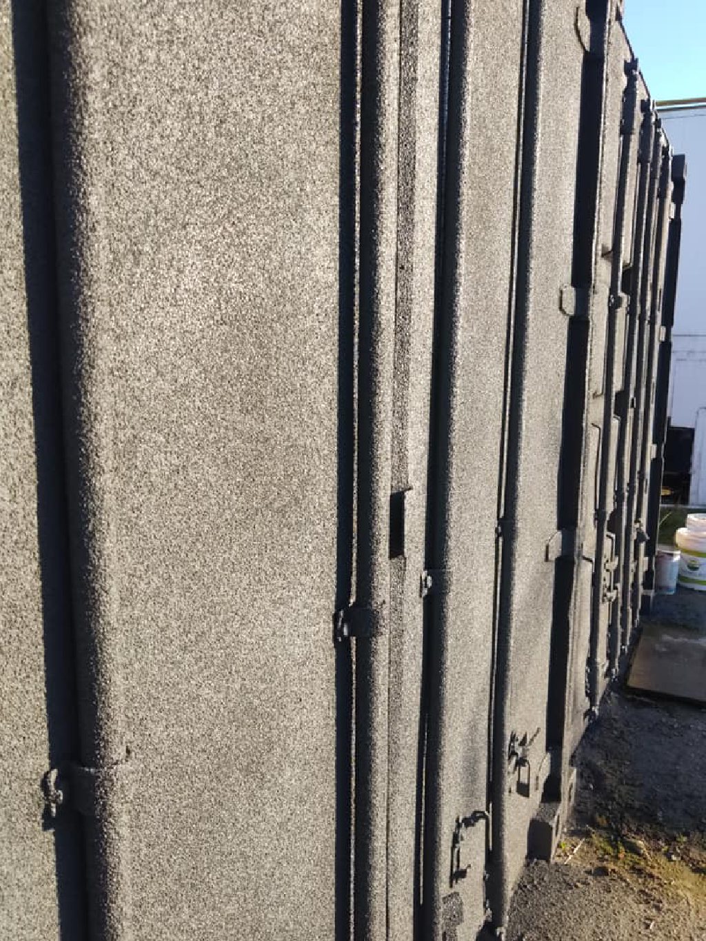The doors end of a container outside, sprayed grey over the leaves, hinges and locking bars