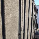The doors end of a container outside, sprayed grey over the leaves, hinges and locking bars