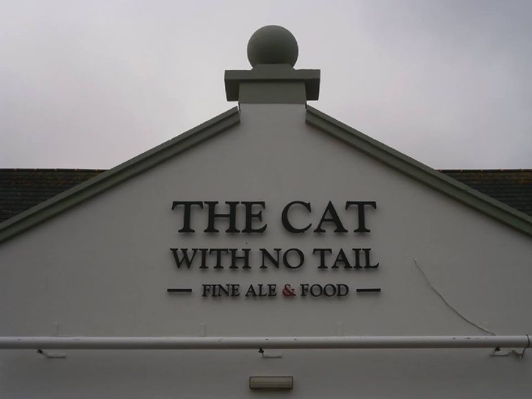 Close view of the gable apex, raised lettering and the ball finial against a grey sky