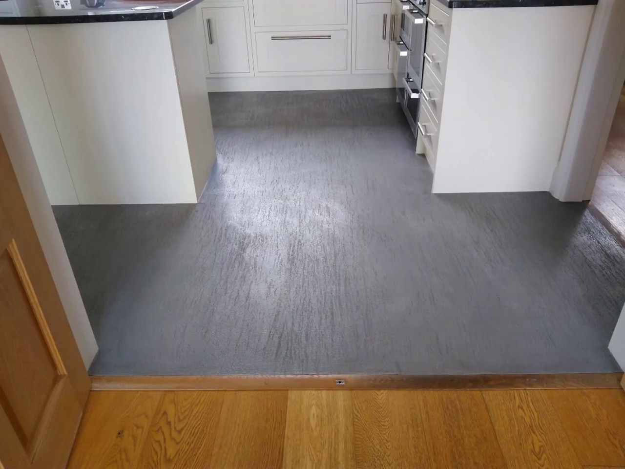 A seamless grey MicroCement floor running through a doorway and meeting an oak threshold